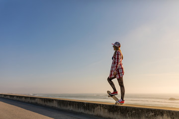 Cute girl with skateboard near the beach at sunset