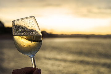 Female hand with a glass of white wine on the background of a beautiful sunset.  Travel vacations concept.