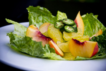Vibrant peach salad close-up with juicy slices and fresh greens against a dark background — a bold and colorful gourmet dish.