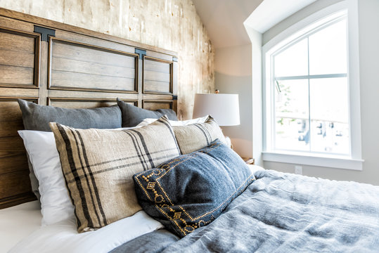 Closeup of new bed comforter with headboard, side table, lamp, decorative pillows in bedroom in staging model home, house or apartment by window with sunlight