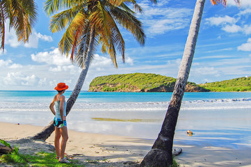Young woman tourist standing under palm tree on beautiful beach on Grenada island, Caribbean region of Lesser Antilles