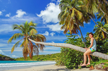 Young woman tourist sitting on palm tree on beautiful La Sagesse beach on Grenada island, Caribbean region of Lesser Antilles