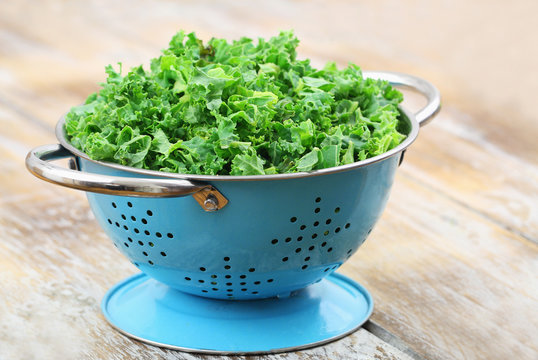 Blue colander with raw shredded kale on rustic wooden surface
