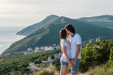 Naklejka premium Man kisses a woman on the cheek and hugs, standing on a mountain with seascape. Side view.