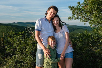 Family portrait mother, father and son on a background of mountains in summer wearing light clothing