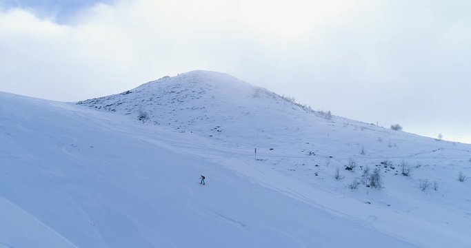 Side aerial over winter snowy mountain ski track field with mountaineering skier people walking up climbing.Snow covered mountains.Fog clouds rising.Winter nature outdoor sport establisher.4k drone