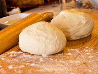 Yeast dough in flour on a wooden board with rolling pin
