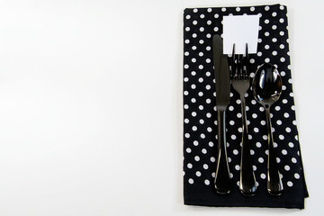 black silverware with blank square paper on fork tine and polka dot napkin on white background