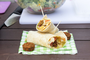 The street food, vegetarian vegetable wrap served on the paper napkin. The green lettuce, tomato,...