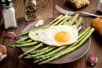 plate with fried egg and asparagus on barbecue on rustic wood
