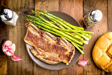 overhead take of grilled barbecue steak with green asparagus, on rustic wood