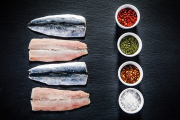 Fresh raw herrings with herbs served on black stone on wooden table