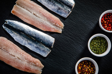Fresh raw herrings with herbs served on black stone on wooden table