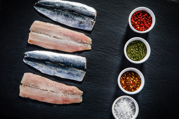 Fresh raw herrings with herbs served on black stone on wooden table