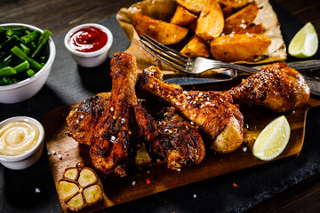 Grilled drumsticks with baked potatoes on wooden background