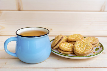 blue mug of tea and sandwich cookies on wooden background 
