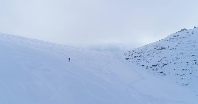 Orbit aerial over winter snowy mountain ski track field with mountaineering skier people walking up climbing.Snow covered mountains.Fog clouds rising.Winter nature outdoor sport establisher.4k drone