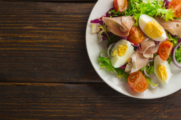 Fresh salad with mixed greens and cherry tomato in bowl on wooden background