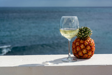 One glass of cold white wine and baby pineapple served on outdoor terrace with sea view