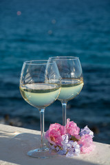 Two glasses with cold white wine served outside on terrace with pink tropical flowers, luxury resort with sea view, romantic vacation