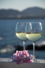 Two glasses with cold white wine served outside on terrace with pink tropical flowers, luxury resort with sea view, romantic vacation