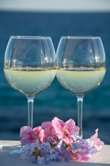 Two glasses with cold white wine served outside on terrace with pink tropical flowers, luxury resort with sea view, romantic vacation
