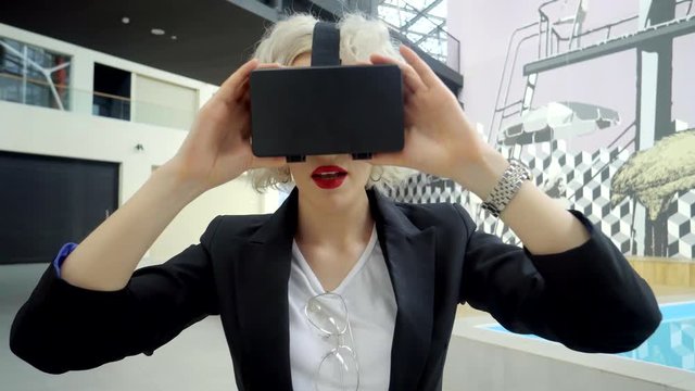 Amazing blonde woman is trying a vr headset on indoor. She is experiencing a virtual reality with a technology.