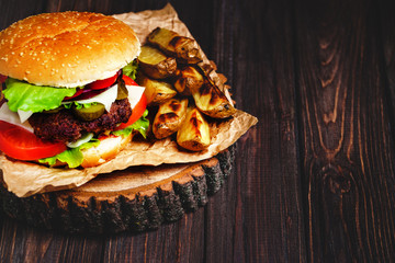 Closeup of home made beef burgers with lettuce and mayonnaise served on little wooden cutting board. Dark background