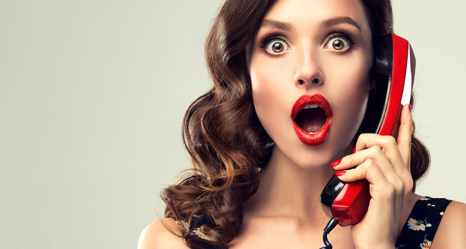 Beautiful woman in pin up style with vintage red phone.  Shocked pretty girl  . Presenting your product. Expressive facial expressions