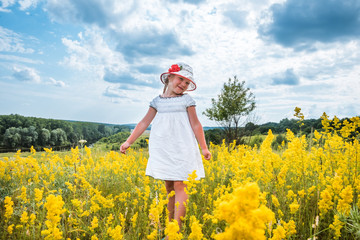 Fototapeta premium Cute little laughing girl walking in field of yellow flowers