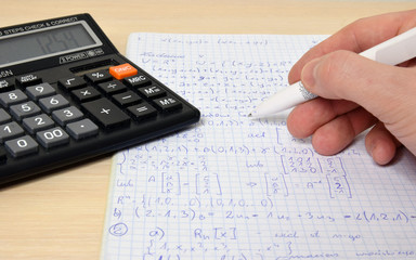 Solving math problems. Calculator, pen, hand.