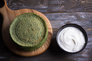 Wooden board with a stack of spinach pancakes and sour cream on the wooden table, rustic style, selective focus © olepeshkina