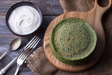 Spinach pancakes with sour cream on a wooden board, rustic style, selective focus