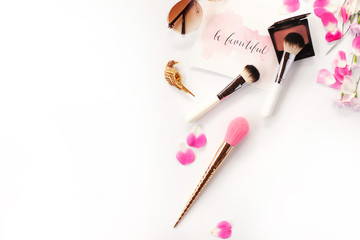 Top view of cosmetics and female accessories on white with pink petals and inspirational words written in calligraphy style `Be beautiful`. Beauty blog flat lay concept.