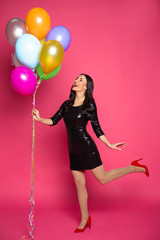 Obraz na płótnie Canvas Girl with helium balloons. Beautiful smiling stylish woman in a little black dress with colorful helium balloons on a pink background.