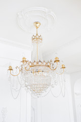 Expensive interior. Large electric chandelier made of transparent glass beads. White ceiling decorated with stucco molding. White patterned. Mouldings element from gypsum.
