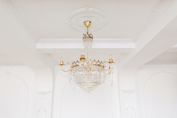 Expensive interior. Large electric chandelier made of transparent glass beads. White ceiling decorated with stucco molding. White patterned. Mouldings element from gypsum.