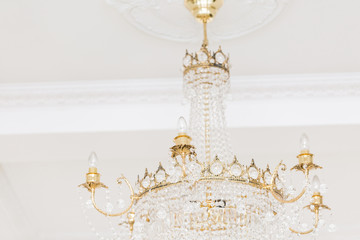 Expensive interior. Large electric chandelier made of transparent glass beads. White ceiling decorated with stucco molding. White patterned. Mouldings element from gypsum.