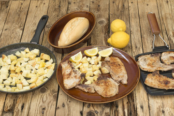 Un plato con chuletas de cerdo y patatas, una sartén con las patatas fritas y otra con las...