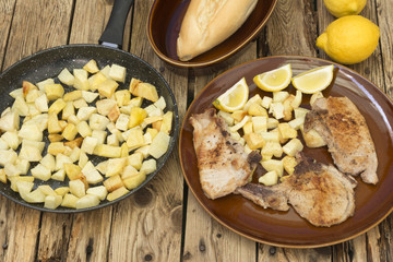 Un plato de chuletas con patatas, una sartén con patatas fritas