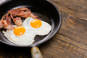 Bacon and Egg. Salted egg and sprinkled with black pepper. English breakfast. Grilled bacon, two eggs on pan on wooden table.