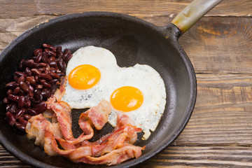 Bacon,Egg and bean. Salted egg and sprinkled with black pepper. English breakfast. Grilled bacon, two eggs and beans in pan on wooden table