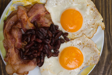Plate with scrambled eggs, bacon and beans on a wooden rustic table.
