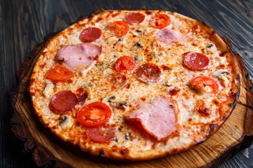 Appetizing sicilian pizza with ham, salami and tomatoes served on wood. Italian food, restaurant or pizzeria menu concept