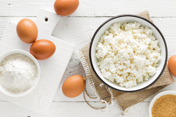 Culinary background with ingredients for cooking, cottage cheese, baking flour, sugar and eggs on white wooden rustic table, top view