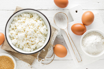 Culinary background with ingredients for cooking, cottage cheese, baking flour, sugar and eggs on white wooden rustic table, top view