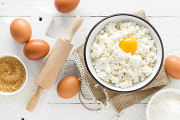 Culinary background with ingredients for cooking, cottage cheese, baking flour, sugar and eggs on white wooden rustic table, top view