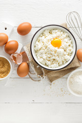 Culinary background with ingredients for cooking, cottage cheese, baking flour, sugar and eggs on white wooden rustic table, top view