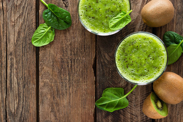 Kiwi smoothie drink of spinach leaves and fresh fruits on wooden rustic table, healthy detox diet