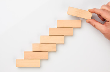 Man hand put wooden blocks in the shape of a staircase isolated on white background with copy space. Concept of building success foundation